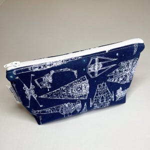 May include: A blue zippered pouch with a white zipper and a white print of various Star Wars spaceships on a dark blue background.