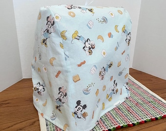 May include: A light blue kitchen appliance cover with a Mickey Mouse and Minnie Mouse breakfast themed print. The print features Mickey and Minnie Mouse, eggs, bacon, croissants, donuts, milk cartons, and other breakfast foods.