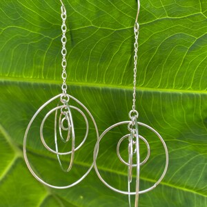 May include: Silver dangle earrings with multiple interlocking circles. The earrings are suspended from a delicate chain.