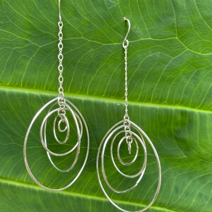 May include: Silver dangle earrings with four interlocking circles. The circles are of varying sizes and are connected by a delicate chain.
