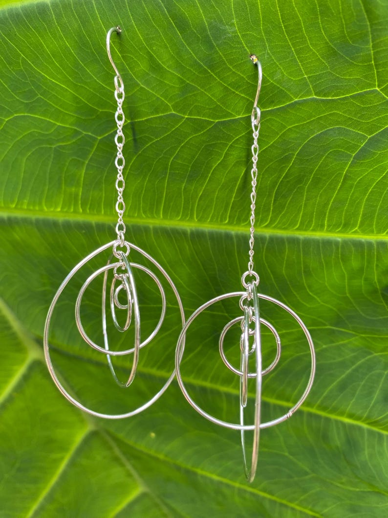 May include: Silver dangle earrings with multiple interlocking circles. The earrings are suspended from a delicate chain.