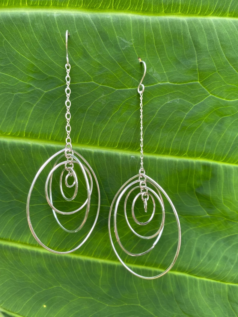 May include: Silver dangle earrings with four interlocking circles. The circles are of varying sizes and are connected by a delicate chain.