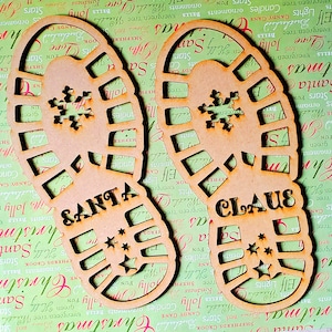 May include: Two wooden Christmas ornaments shaped like footprints. The left ornament says "SANTA" and the right ornament says "CLAUS". Both ornaments have a snowflake design and a star pattern.
