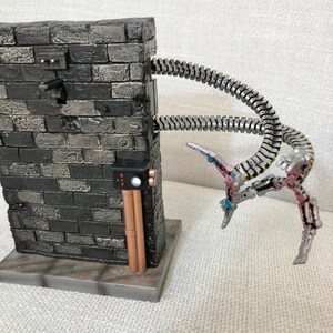 May include: A detailed diorama featuring a brick wall with metallic tentacles extending from it. The tentacles have articulated joints and end in claw-like structures. The wall has electrical components and copper-colored pipes.