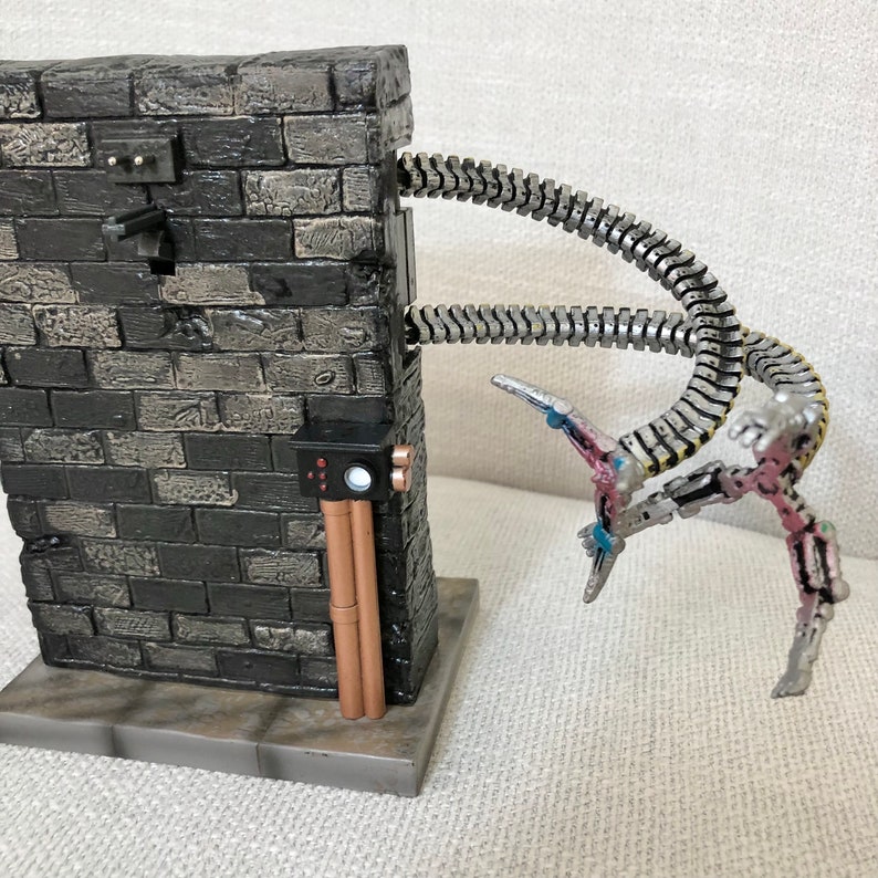 May include: A detailed diorama featuring a brick wall with metallic tentacles extending from it. The tentacles have articulated joints and end in claw-like structures. The wall has electrical components and copper-colored pipes.