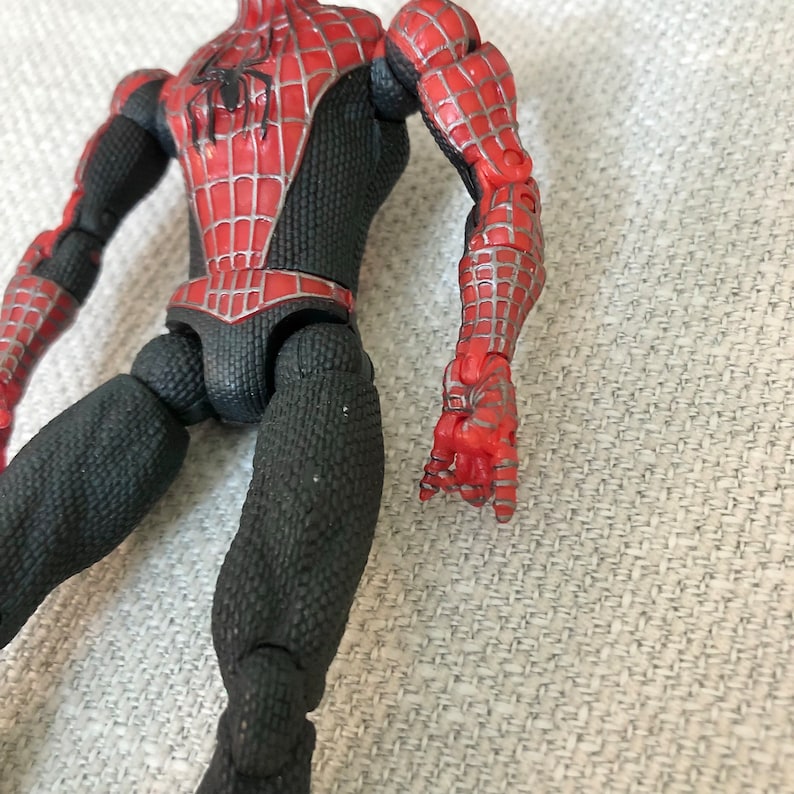 May include: A Spider-Man action figure with a red and black costume. The figure has a detailed design with a web pattern on the red sections. The figure's joints are visible, and the hands are in a gripping pose.