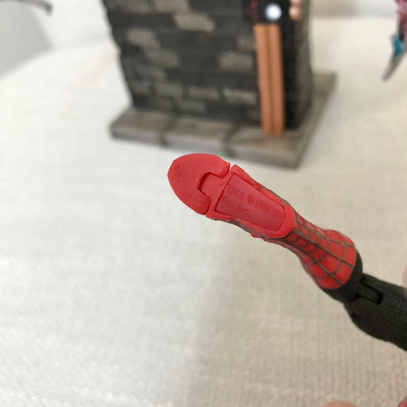 May include: Close-up of a red and black Spider-Man action figure's foot. The foot is red with a textured design and the text "&copy; 1998 Marvel Ent. Inc." is visible. The figure's webbed design is visible on the arm.