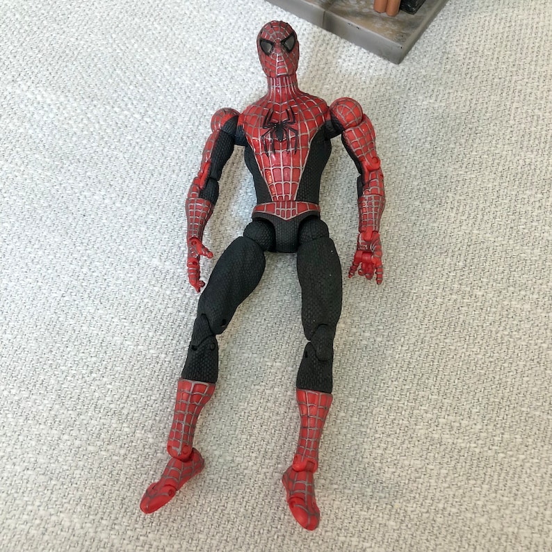 May include: A Spider-Man action figure, featuring a red and black costume with a spider emblem on the chest. The figure has articulated joints and detailed paintwork, showcasing the character's iconic design. The figure is approximately 6 inches tall.