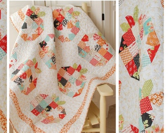 May include: A quilt pattern featuring a patchwork design of pumpkin seeds. The quilt is made with a variety of fabrics in shades of red, orange, green, blue, and white. The quilt is displayed on a white rocking chair. The text "Pumpkin Seeds" is displayed at the bottom of the image. The text "www.thepatternbasket.com" is displayed below the text "Pumpkin Seeds".