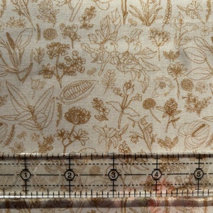 May include: A white fabric with a brown floral pattern. The fabric is measured with a ruler showing 6 inches.