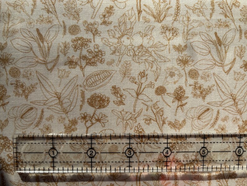 May include: A white fabric with a brown floral pattern. The fabric is measured with a ruler showing 6 inches.
