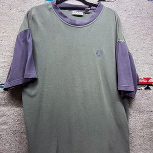 May include: A green and purple short-sleeved t-shirt with a small embroidered logo on the front.