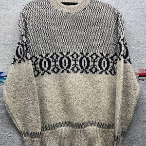 May include: A cream-colored sweater with a black and white geometric pattern. The sweater has a crew neck and long sleeves.