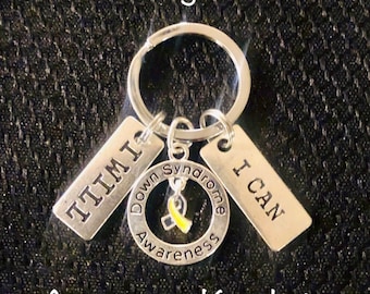 May include: Silver keychain with three tags. One tag says "I CAN", another says "I AM", and the third tag says "Down Syndrome Awareness". The tag with the awareness message has a yellow ribbon.