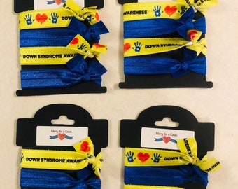 May include: Four packages of colorful hair ties with the words "Down Syndrome Awareness" and "Rome Awareness" printed on them. The hair ties are blue and yellow with a red heart and handprint design.