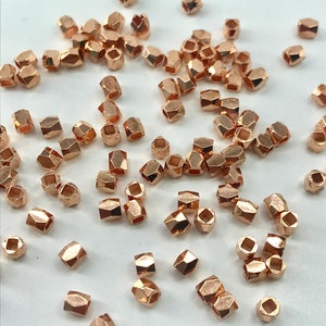 May include: A scattering of small, rose gold-colored, faceted beads. The beads are hexagonal in shape and have a slightly irregular, hammered finish.