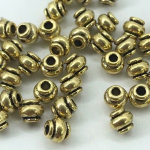 May include: A group of gold-toned metal beads with a decorative grooved design. The beads are round and have a hole in the center for stringing.