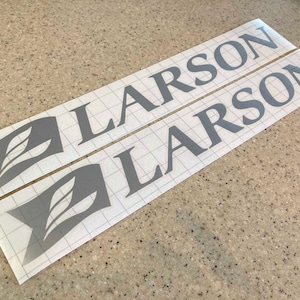 May include: Two gray vinyl decals with the word "LARSON" printed in a bold, sans-serif font. Each decal features a stylized leaf design.