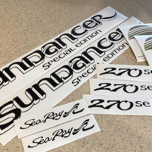 May include: A set of black and white vinyl decals for a boat. The decals include the words "Sundancer Special Edition" and "Sea Ray" along with the number "270 se".