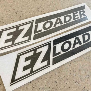May include: Two white stickers with black text that reads "EZ LOADER" in a bold, sans-serif font. The stickers are rectangular and have a black border.