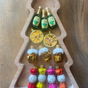 May include: A set of 10 Christmas ornaments in a wooden tree-shaped tray. The ornaments are glass and feature a variety of designs, including wine bottles, lemons, beer mugs, and candy canes. The ornaments are all in various colors, including green, yellow, red, orange, and white.