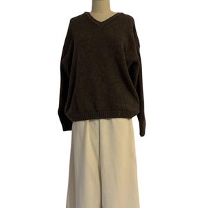 May include: A dark brown V-neck sweater with long sleeves and a ribbed hem, paired with wide-leg off-white trousers. The sweater features a textured knit pattern, while the trousers have a clean, straight-cut design and a flat front waistband.