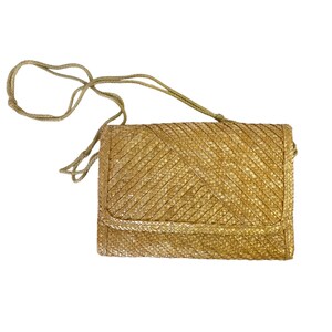 Peut inclure: Un sac à bandoulière en paille tressée avec une longue bandoulière. Le sac est de couleur brun clair et a une forme rectangulaire.