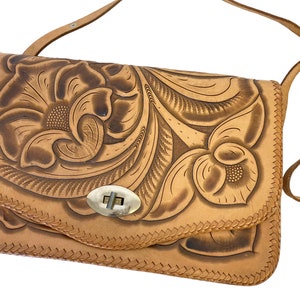 Peut inclure: Un sac &agrave; bandouli&egrave;re en cuir tann&eacute; avec un motif floral cisel&eacute; et un fermoir en laiton.