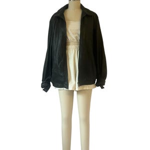 May include: A black zip-up jacket with a collar, paired with a white crop top and shorts. The outfit is displayed on a mannequin. The jacket has long sleeves and a slightly textured appearance.