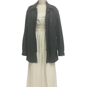 Puede incluir: Una chaqueta de cuero negra con cuello y cierre de botones, combinada con un top color crema y pantalones de pierna ancha. La chaqueta tiene mangas largas y un diseño clásico, adecuada para varios conjuntos.