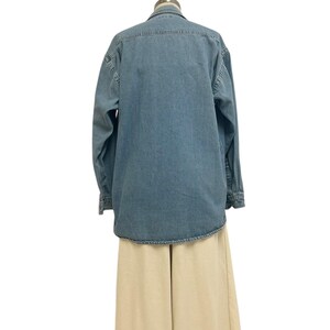 Op de afbeelding: Een lichtblauw denim overhemd met lange mouwen en een knoopsluiting. Het overhemd wordt gecombineerd met een beige broek met wijde pijpen. De kleding wordt gepresenteerd op een mannequin tegen een witte achtergrond.