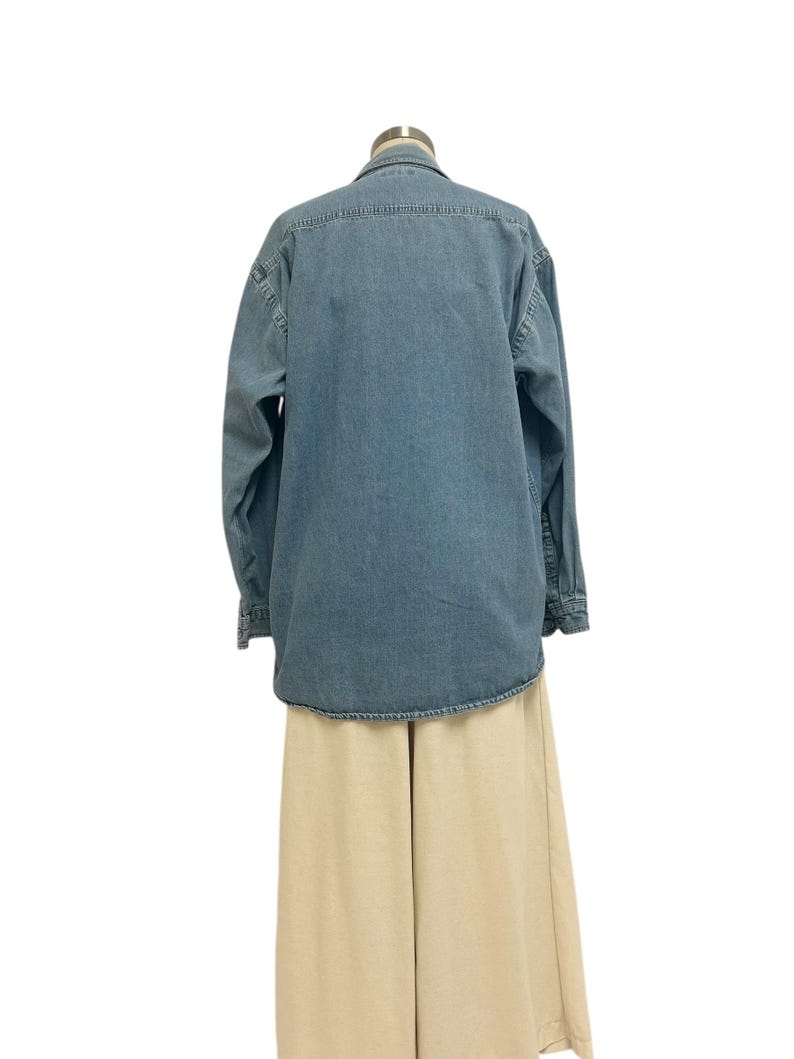 Op de afbeelding: Een lichtblauw denim overhemd met lange mouwen en een knoopsluiting. Het overhemd wordt gecombineerd met een beige broek met wijde pijpen. De kleding wordt gepresenteerd op een mannequin tegen een witte achtergrond.