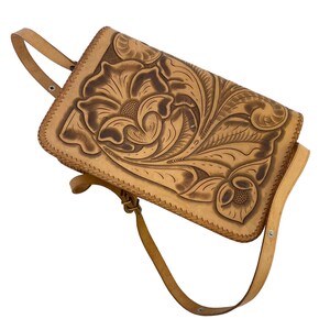 Peut inclure: Un sac &agrave; main en cuir tann&eacute; avec un motif floral en relief sur le devant. Le sac a une longue bandouli&egrave;re et une fermeture &agrave; rabat.