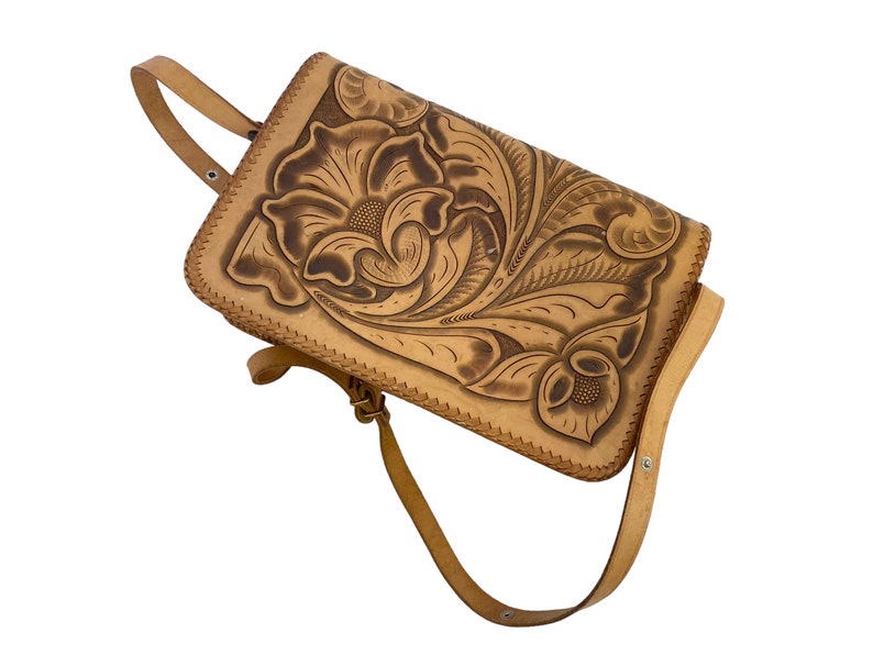 Peut inclure: Un sac &agrave; main en cuir tann&eacute; avec un motif floral en relief sur le devant. Le sac a une longue bandouli&egrave;re et une fermeture &agrave; rabat.