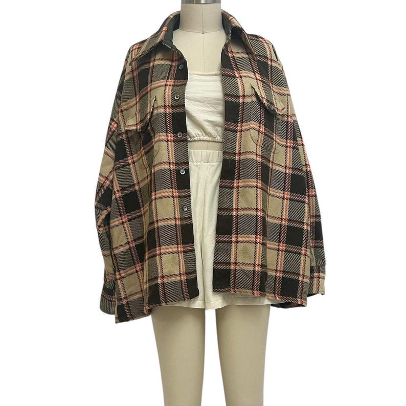 May include: A plaid flannel shirt in shades of black, tan, and red, displayed on a mannequin. The shirt has a collared neckline, button-down front, and two chest pockets. The shirt is layered over a white top and shorts.