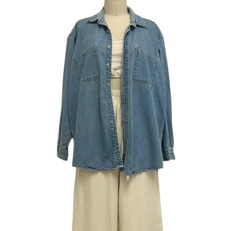 Op de afbeelding: Een lichtblauw spijkeroverhemd met twee borstzakken en een knoopsluiting. Het overhemd wordt gedragen over een cr&egrave;mekleurige top en gecombineerd met een beige broek. De outfit wordt gepresenteerd op een mannequin.