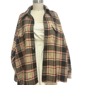May include: A vintage plaid shirt in brown, black, tan, and red. The shirt has a collared neckline, button-down front, and two chest pockets. The shirt is displayed on a mannequin.