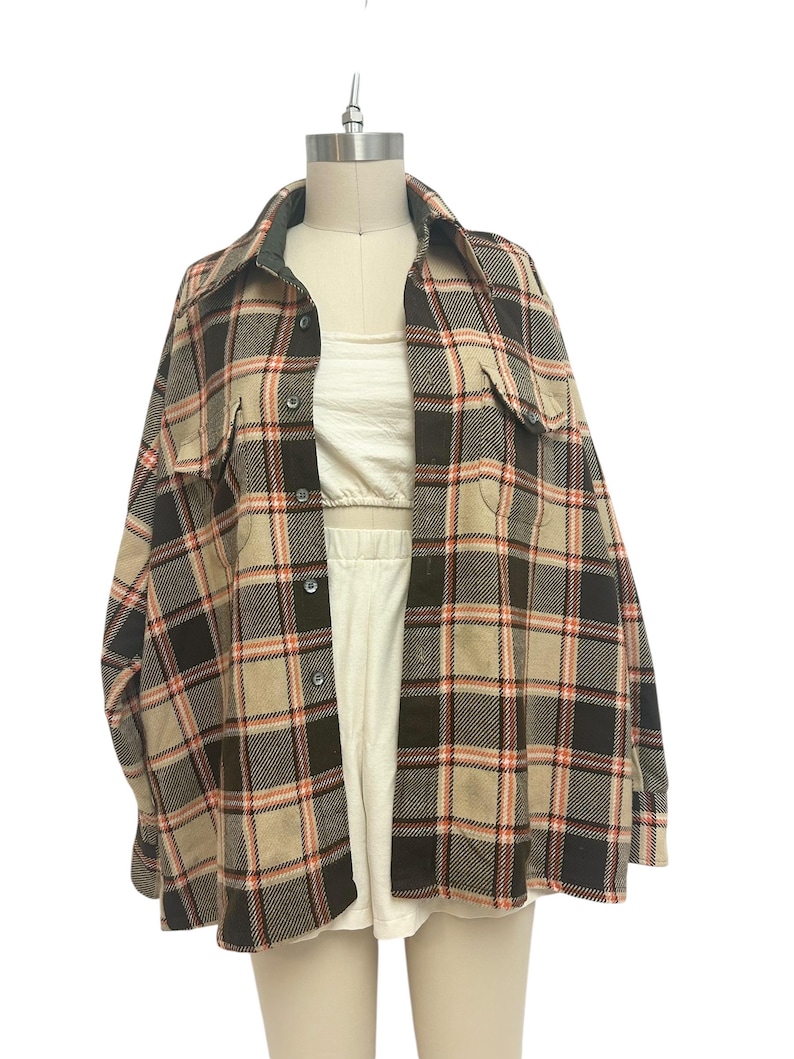 May include: A vintage plaid shirt in brown, black, tan, and red. The shirt has a collared neckline, button-down front, and two chest pockets. The shirt is displayed on a mannequin.