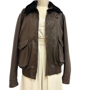 Puede incluir: Chaqueta bomber de cuero marr&oacute;n con cuello de piel sint&eacute;tica negra. La chaqueta tiene dos bolsillos delanteros y un dobladillo acanalado. La chaqueta se exhibe en un maniqu&iacute;. Estilo cl&aacute;sico.