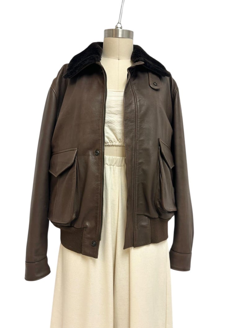 Puede incluir: Chaqueta bomber de cuero marr&oacute;n con cuello de piel sint&eacute;tica negra. La chaqueta tiene dos bolsillos delanteros y un dobladillo acanalado. La chaqueta se exhibe en un maniqu&iacute;. Estilo cl&aacute;sico.