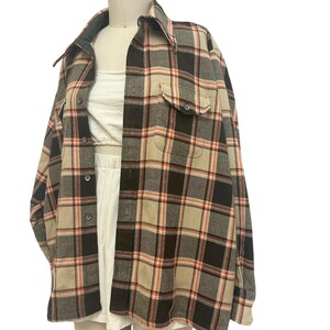 May include: A plaid button-up shirt in a neutral color palette of tan, brown, and orange. The shirt features a collared neckline, two chest pockets, and long sleeves. The garment is displayed on a mannequin.