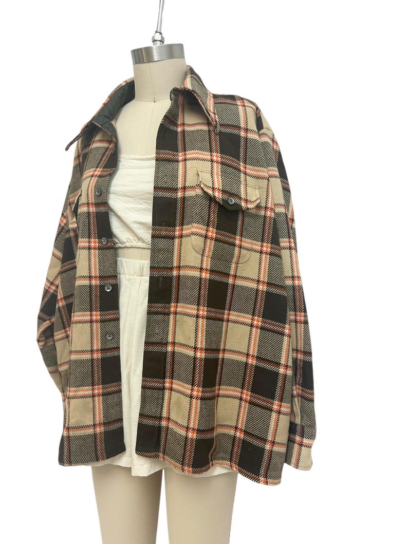 May include: A plaid button-up shirt in a neutral color palette of tan, brown, and orange. The shirt features a collared neckline, two chest pockets, and long sleeves. The garment is displayed on a mannequin.