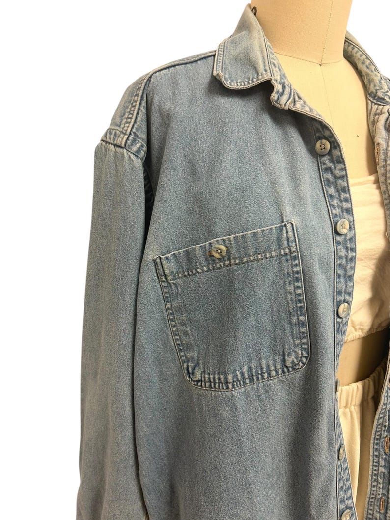 Op de afbeelding: Lichtblauwe spijkerblouse met een knoopsluiting, een enkele borstzak en een klassieke kraag. De blouse heeft lange mouwen en lichte slijtage rond de kraag en manchetten. De blouse wordt op een mannequin getoond.