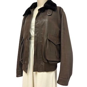Puede incluir: Chaqueta bomber de cuero marr&oacute;n con cuello de piel negra. La chaqueta tiene dos bolsillos delanteros y un dobladillo acanalado. La chaqueta se exhibe en un maniqu&iacute;.