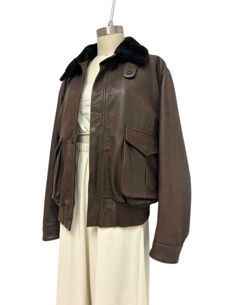 Puede incluir: Chaqueta bomber de cuero marr&oacute;n con cuello de piel negra. La chaqueta tiene dos bolsillos delanteros y un dobladillo acanalado. La chaqueta se exhibe en un maniqu&iacute;.
