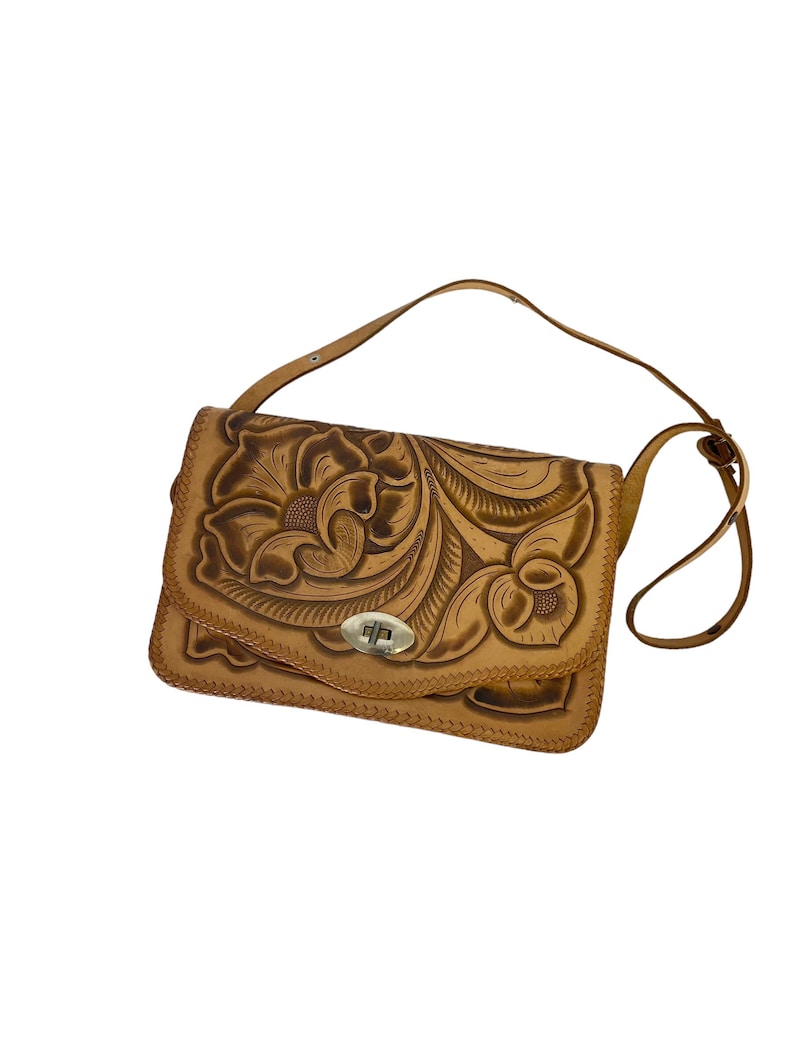 Peut inclure: Un sac &agrave; bandouli&egrave;re en cuir tann&eacute; avec un motif floral cisel&eacute;. Le sac a une fermeture &agrave; rabat avec un fermoir en m&eacute;tal.
