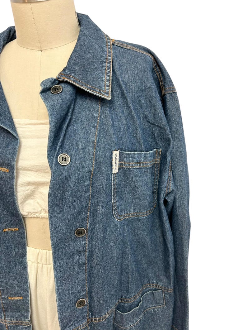 May include: A blue denim jacket with a button-up front and a single chest pocket. The jacket has a label that reads "ZARA" on the pocket.