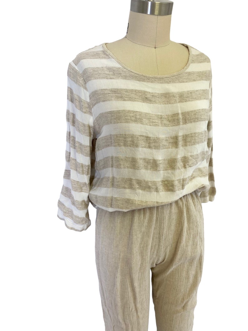 Puede incluir: Una camisa de manga larga a rayas y pantalones a juego en una combinaci&oacute;n de colores beige y blanco. La camisa tiene un escote redondo y los pantalones tienen un corte holgado.
