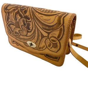 Peut inclure: Un sac &agrave; bandouli&egrave;re en cuir tann&eacute; avec un motif floral gaufr&eacute; dans le cuir. Le sac a une fermeture &agrave; rabat avec un fermoir en m&eacute;tal.