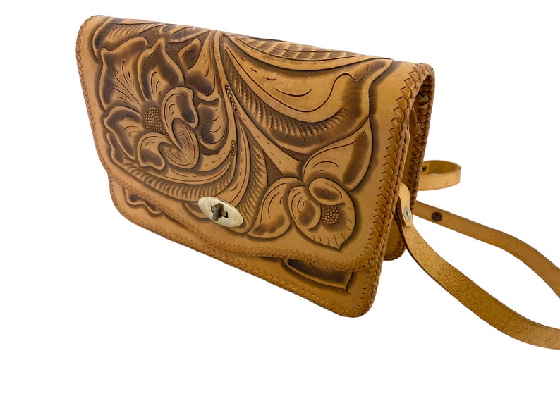 Peut inclure: Un sac &agrave; bandouli&egrave;re en cuir tann&eacute; avec un motif floral gaufr&eacute; dans le cuir. Le sac a une fermeture &agrave; rabat avec un fermoir en m&eacute;tal.